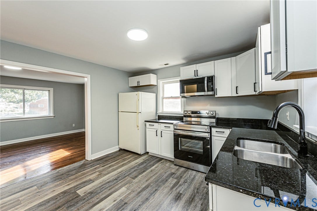 Kitchen featuring white cabinetry, dark stone countertops, stainless steel appliances, and wood-finish flooring