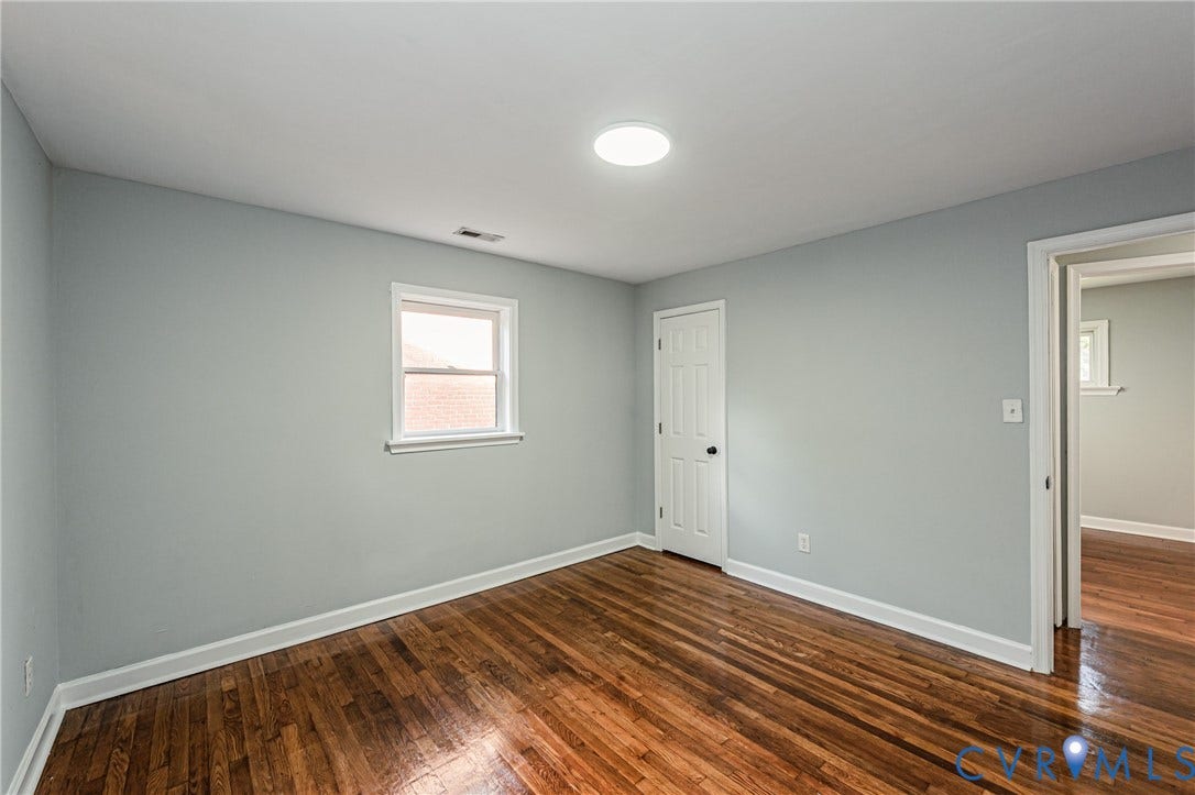 Wood-finish flooring, light gray walls, single window, white trim, and white interior doors
