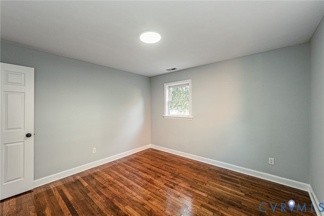 Hardwood flooring, light gray wall finish, recessed ceiling light, white trim, and a paneled door