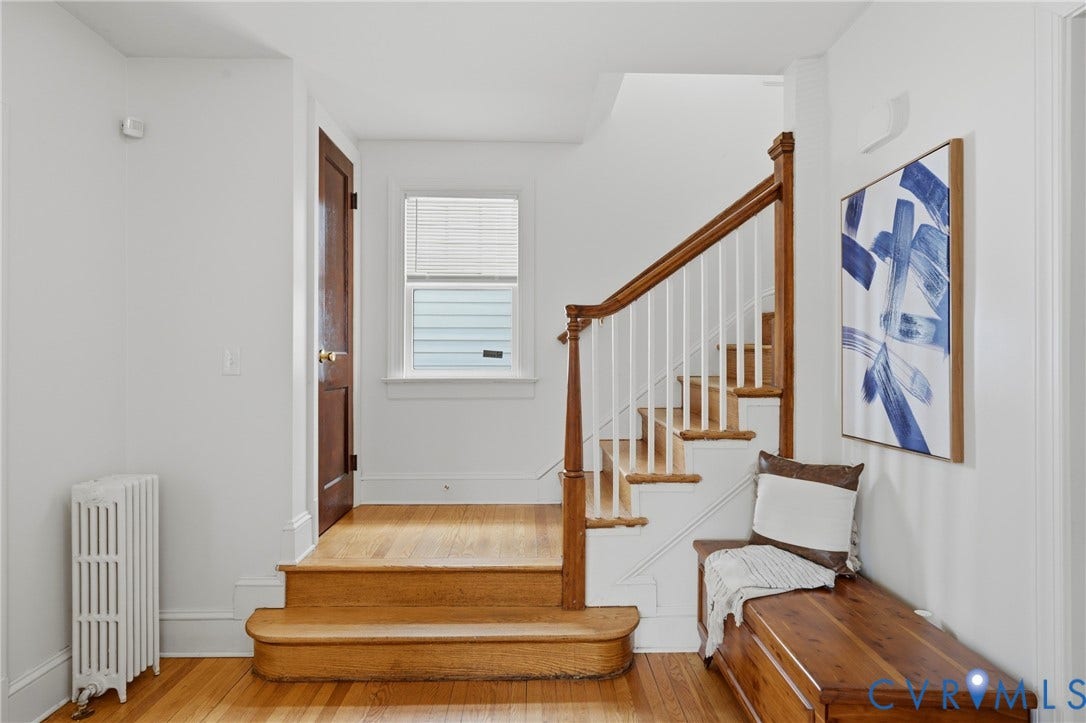 Hardwood flooring, painted white walls, wood staircase with white balusters, natural light window, and dark wood door