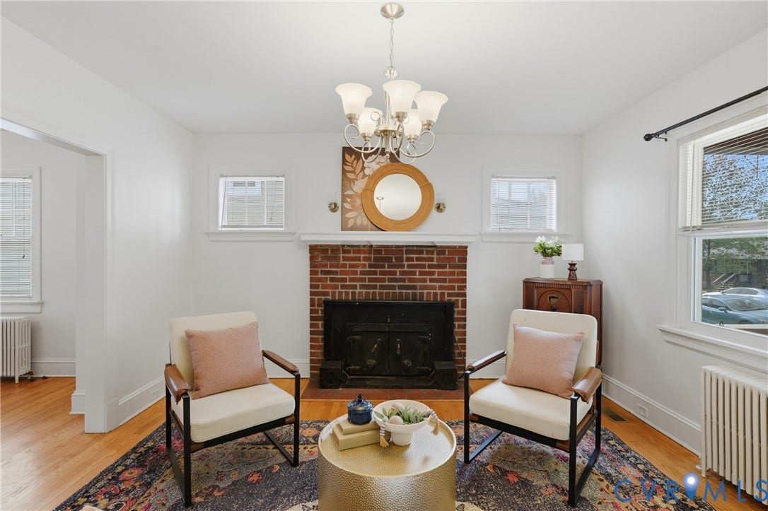 Brick fireplace, wood-finish flooring, overhead chandelier, multiple windows, white wall finishes