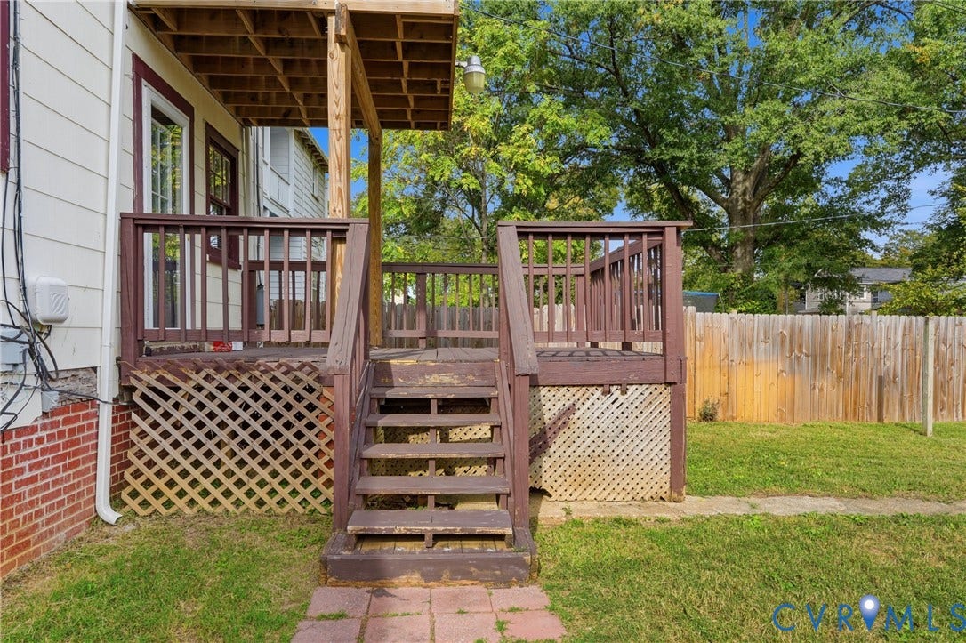 Wooden deck with steps and railing, lattice skirting, and a partial privacy fence