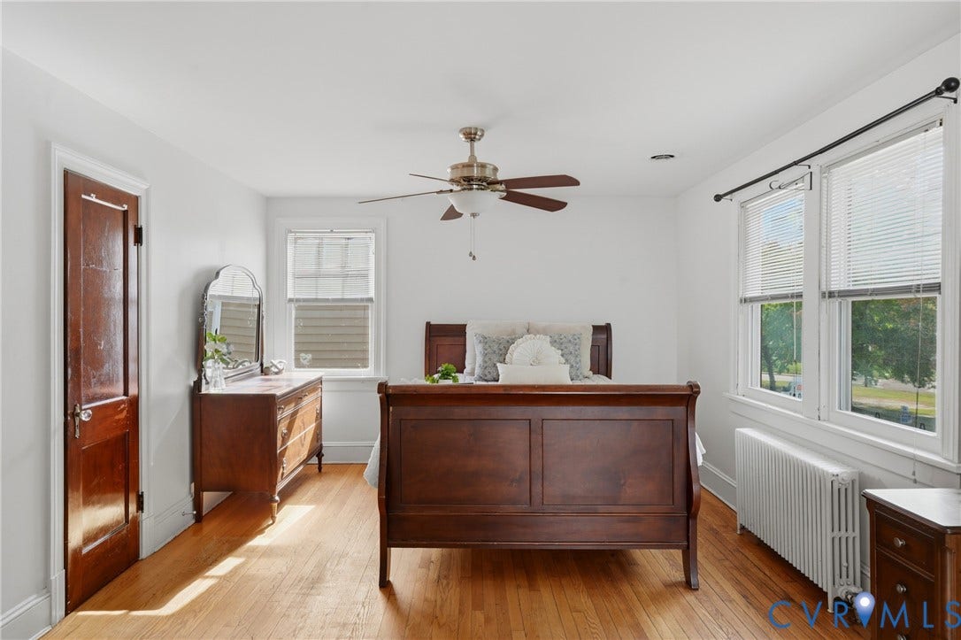 Hardwood flooring, two windows with blinds, ceiling fan, white walls, and a warm wood-tone door