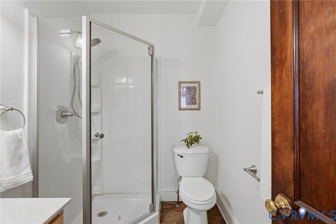 White-tiled shower with glass enclosure, white toilet, and wood-finish door