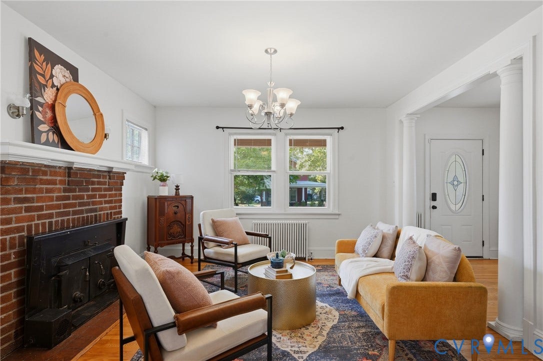 Red brick fireplace with a white mantel, hardwood flooring, and white walls