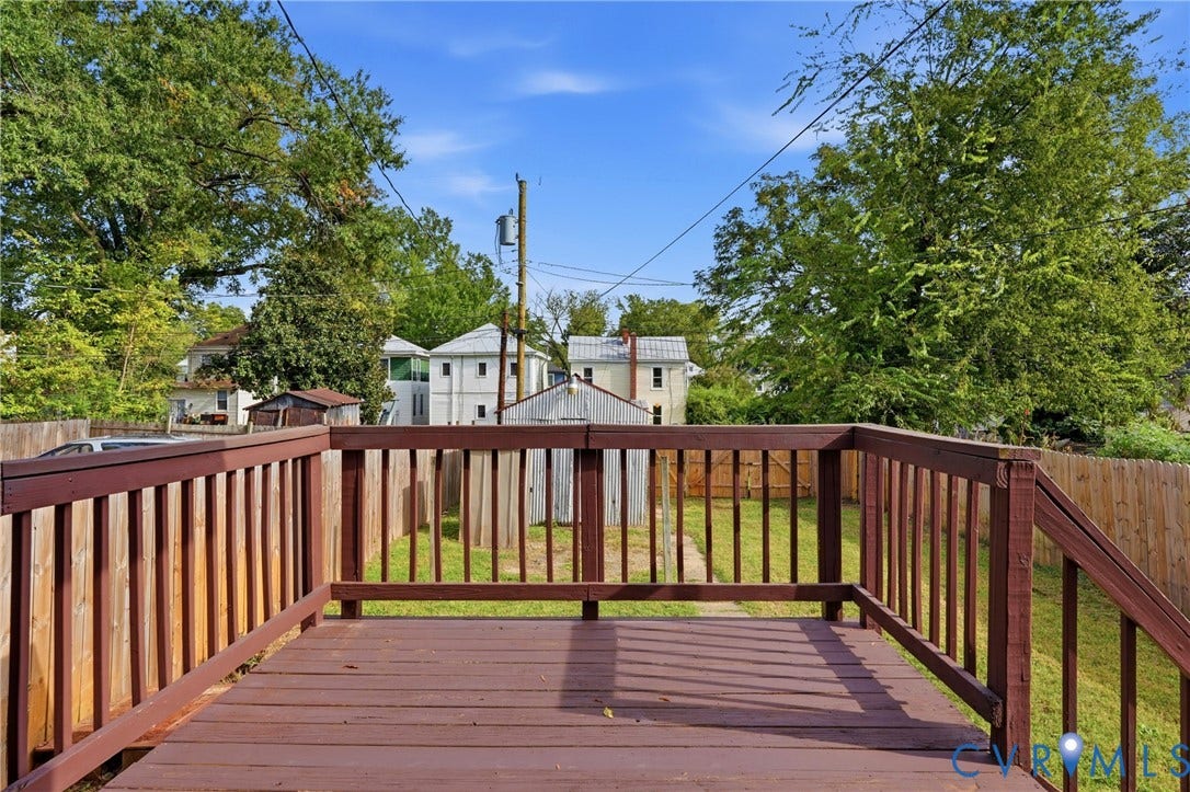 Expansive wood deck with railing overlooking a fenced yard with mature trees
