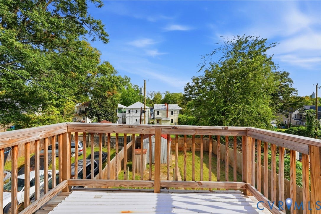 Outdoor deck with wood railings, overlooking a fenced yard and surrounding greenery