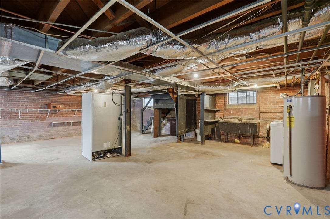 Basement space featuring exposed brick walls, a concrete floor, and utility sink