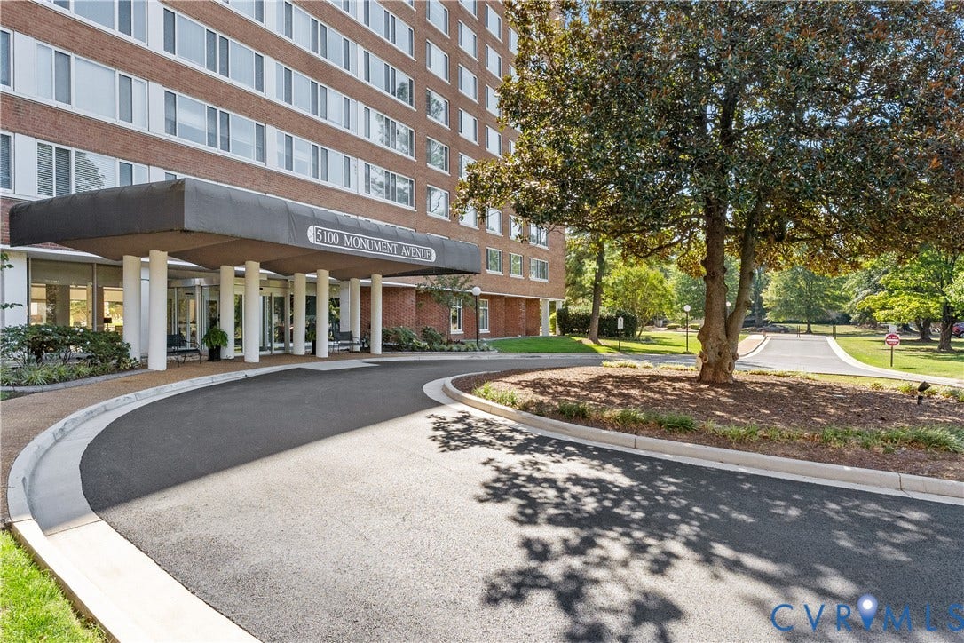 Brick facade high-rise building with a covered entrance, circular driveway, and mature landscaping