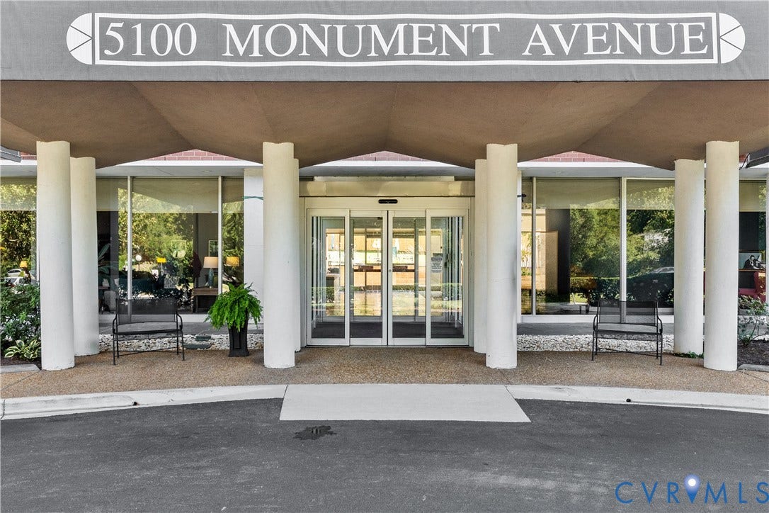 Covered entry with support columns, automated glass doors, and expansive floor-to-ceiling windows