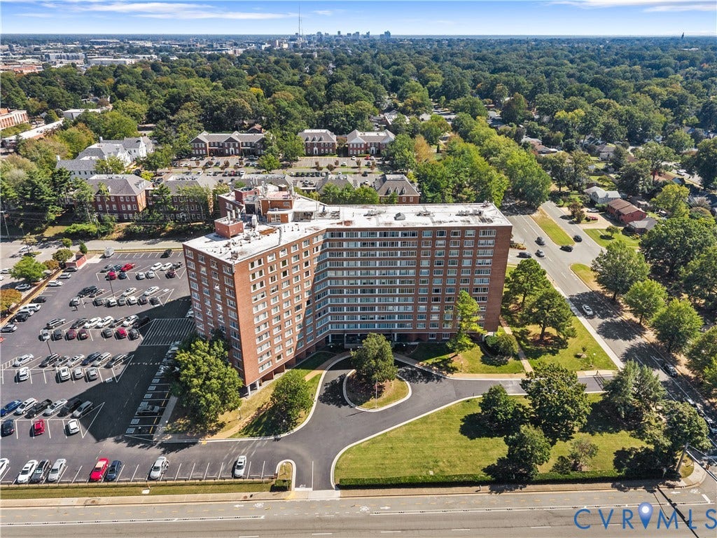 High-rise brick building with multiple balconies, expansive surface parking, circular drive, and surrounding mature trees