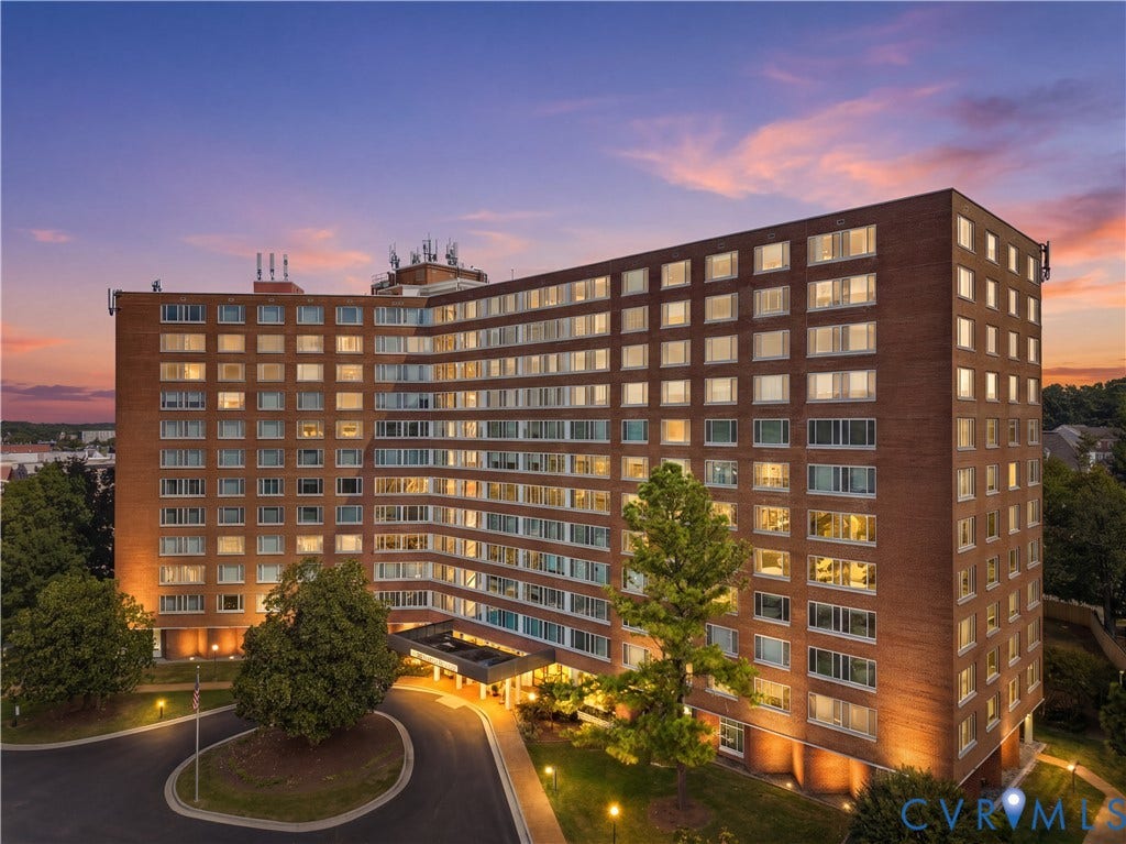 Multi-story brick facade building featuring a covered entrance, exterior lighting, and a circular driveway with landscaping