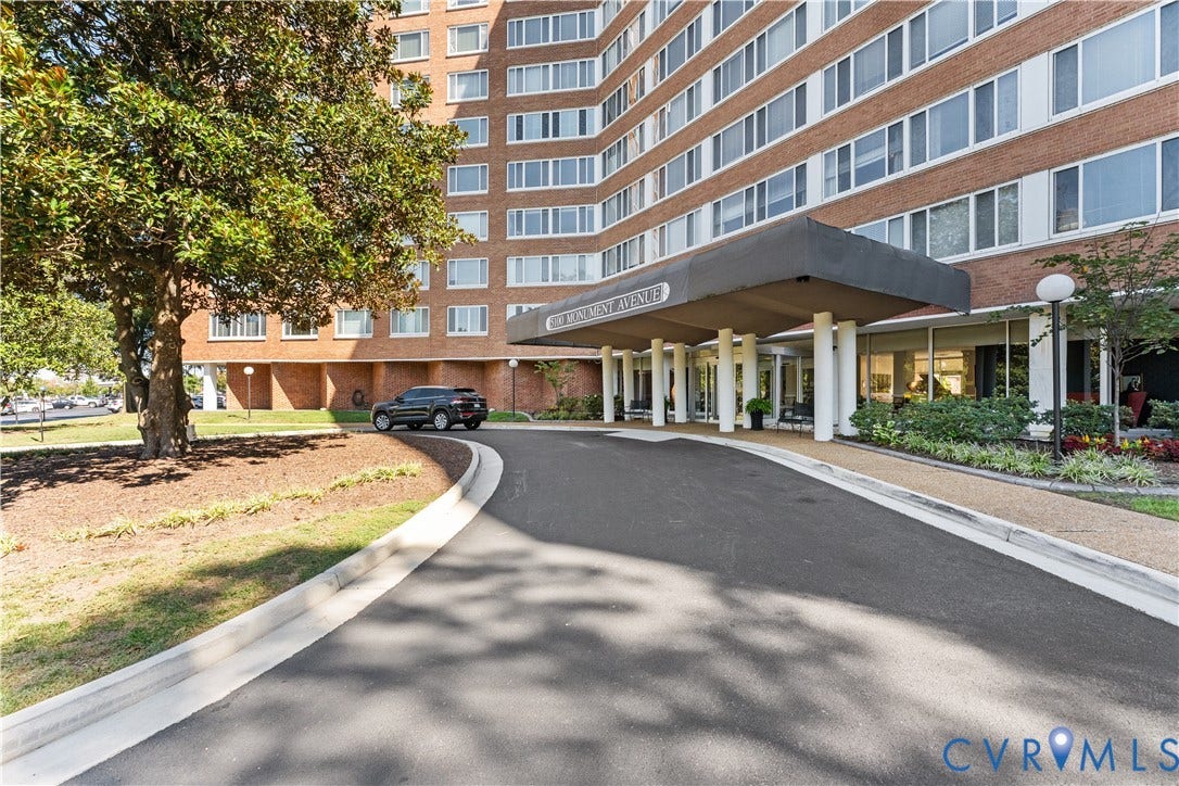 Brick facade building with a covered entryway, mature landscaping, and a paved drive