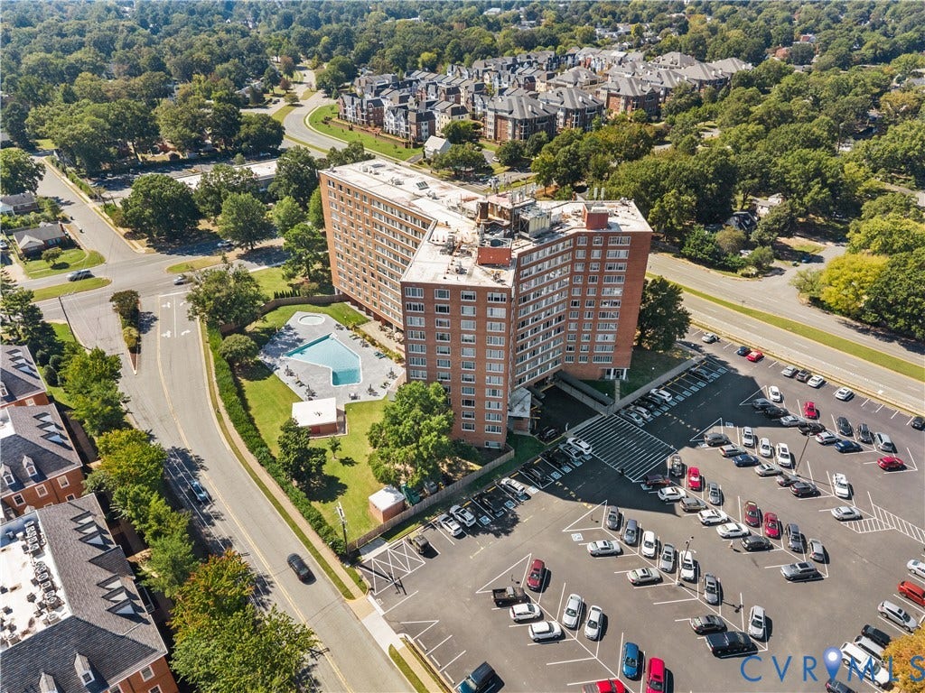 Red brick high-rise building with a surface parking lot, a swimming pool, and surrounding green spaces