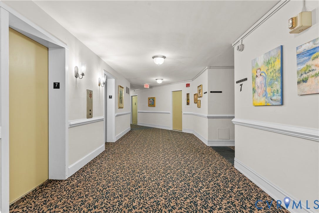 Hallway with patterned carpet flooring, white walls, and wall sconces providing illumination
