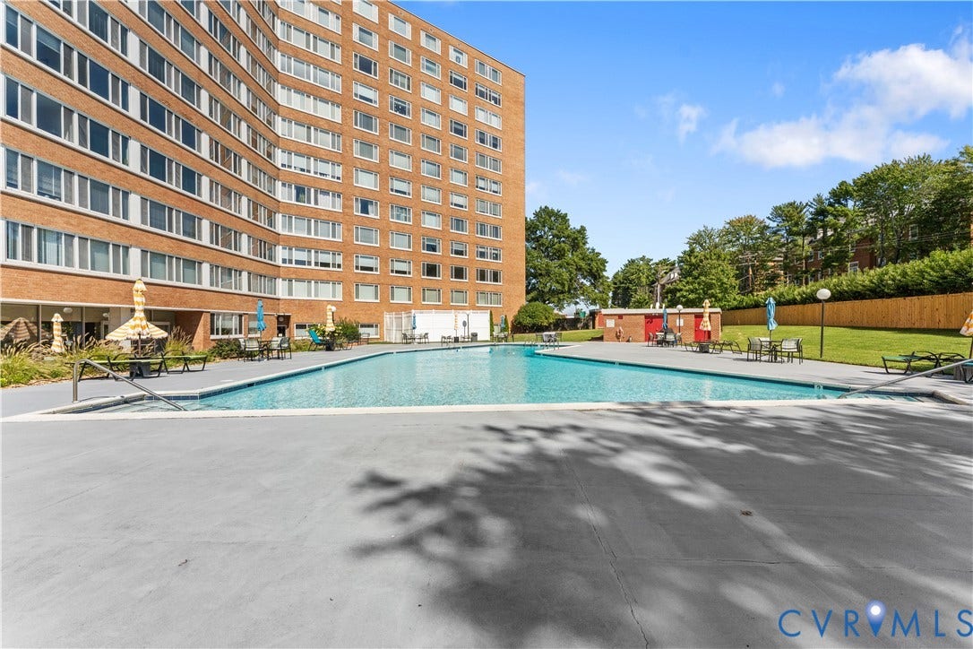 Expansive swimming pool with a surrounding concrete deck, complemented by a manicured lawn area and a large multi-story building exterior