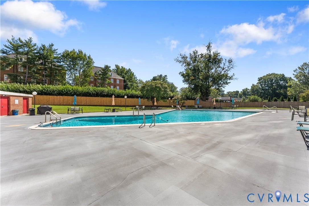 Expansive outdoor swimming pool with surrounding concrete decking, perimeter fencing, and mature landscaping