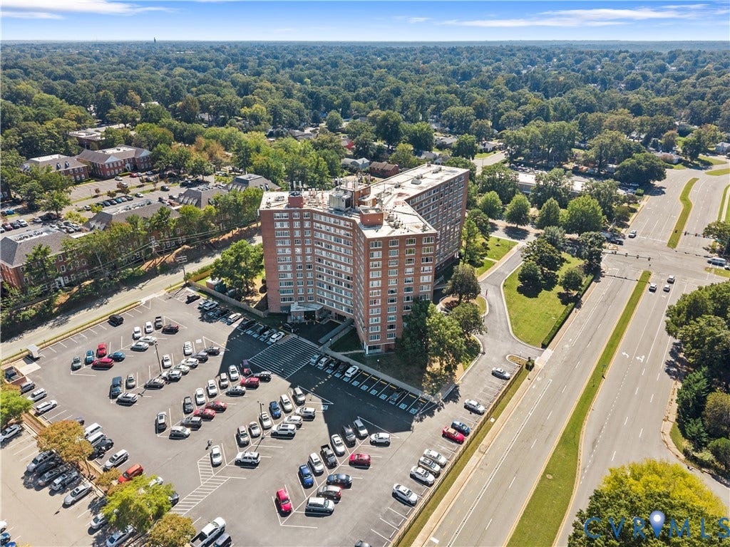 Multi-story brick building with multiple windows, surrounded by paved parking areas and mature landscaping