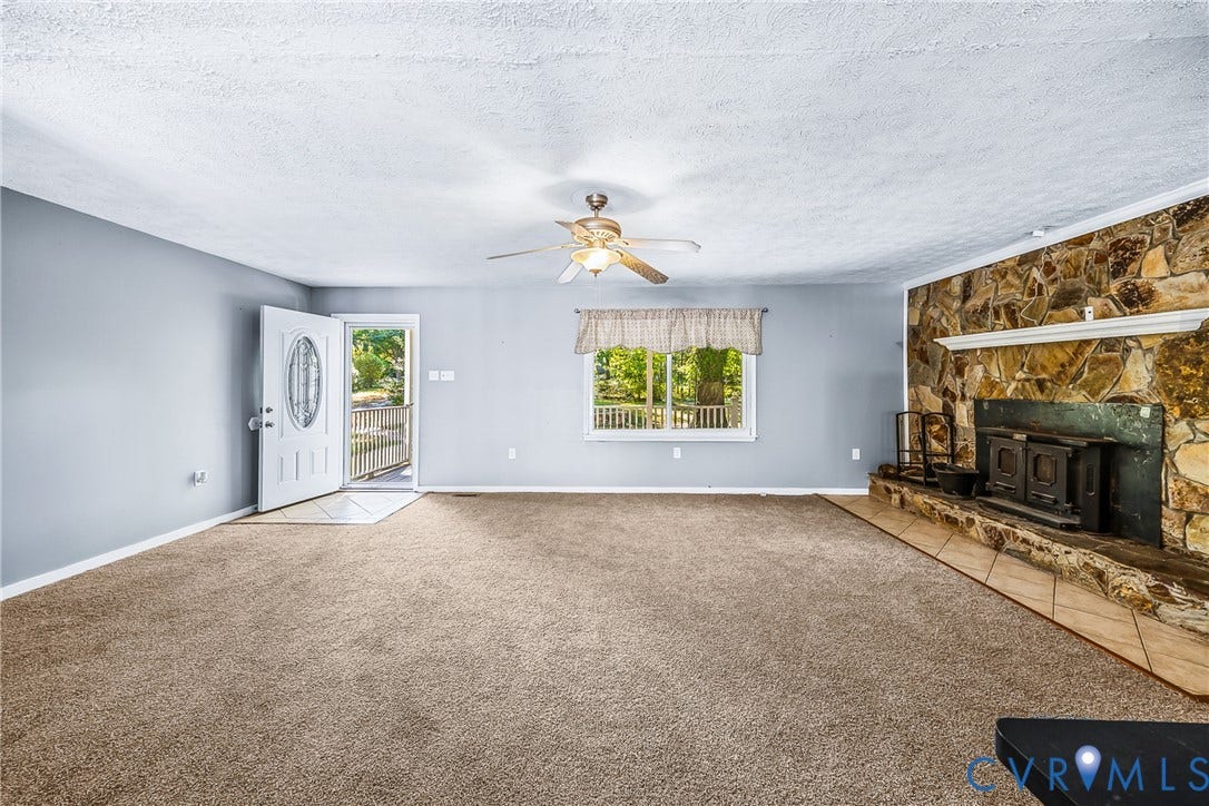 Spacious living area featuring a stone-clad fireplace with a wood-burning insert, an overhead ceiling fan, and a front entry door with an oval glass insert