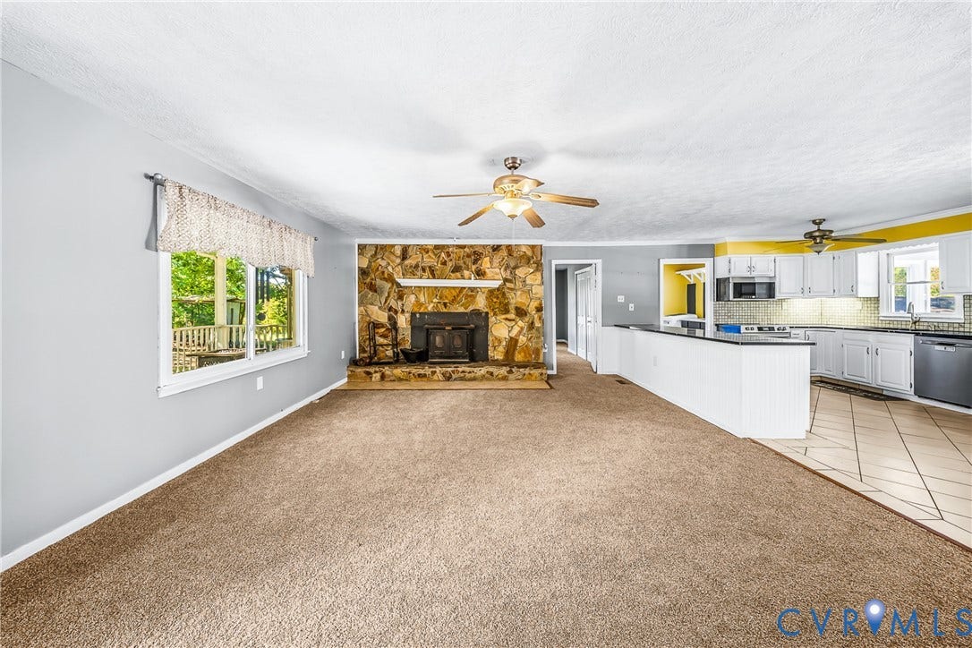 Spacious living area with a stone fireplace, large window, and light carpeting