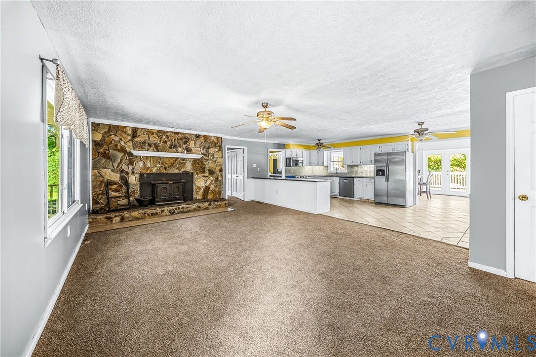 Stone-faced fireplace with hearth, kitchen with white cabinetry and stainless steel appliances, central island, and double French doors to an exterior deck