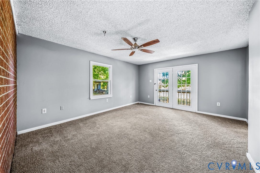 Neutral gray wall paint, textured ceiling, brown brick accent wall, white-framed window, and white-framed French doors