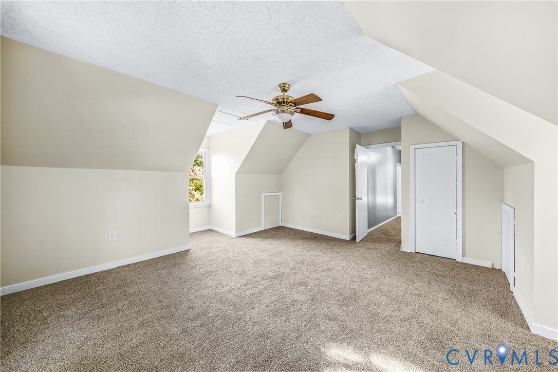 Spacious room with sloped ceilings, carpet flooring, and a ceiling fan with integrated lighting