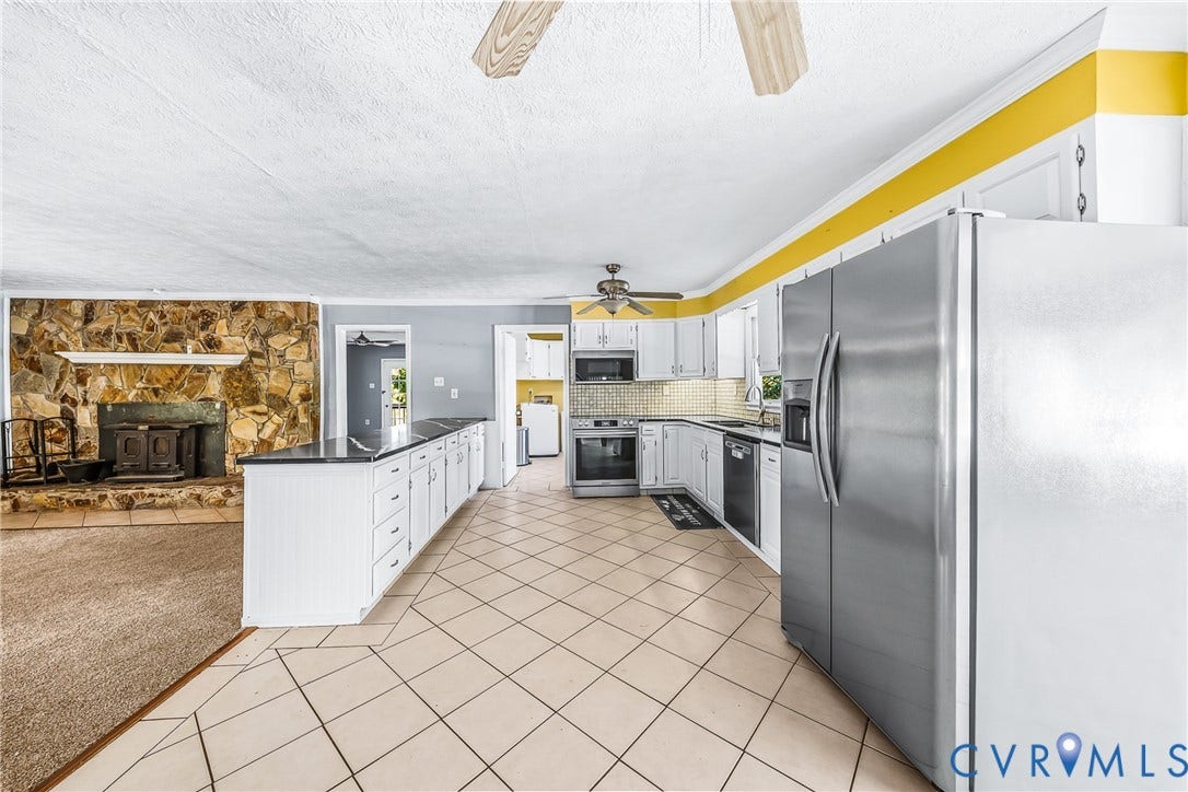 Kitchen featuring white cabinetry, stainless steel appliances, tiled flooring, and a stone-clad fireplace