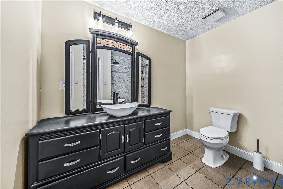Black vanity with ample storage, white vessel sink, and wall-mounted light fixture