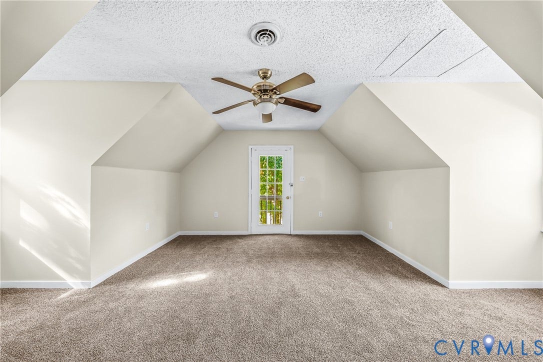 Vaulted ceiling with a ceiling fan, carpeted flooring, and a glass-paneled door