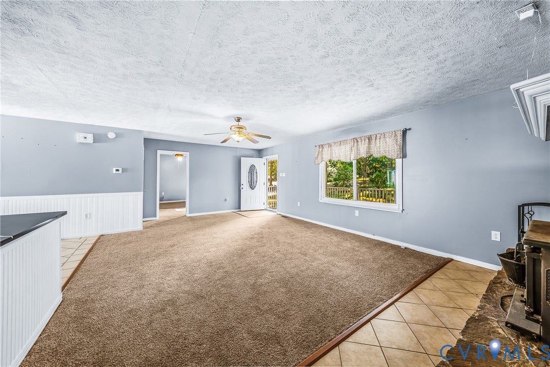 Living area with carpet flooring, light blue walls, white wainscoting, and a ceiling fan