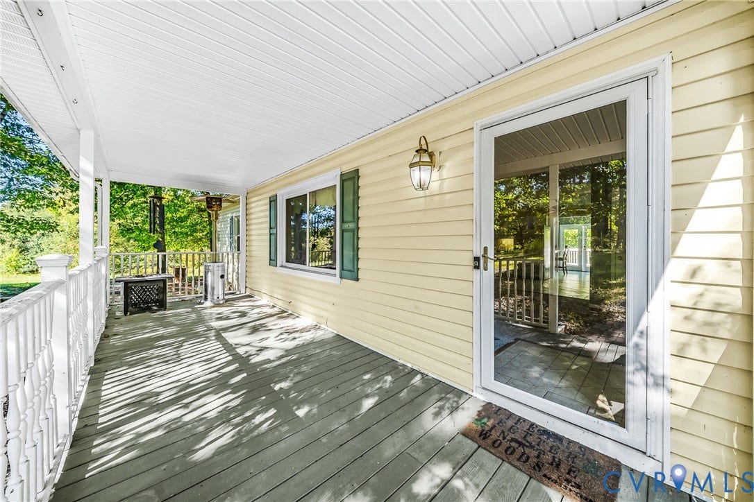 Spacious covered porch with white railing, wood-finish flooring, and light yellow siding