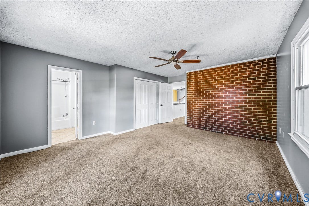 Textured accent wall, wood-finish ceiling fan, wall-to-wall carpeting, white bi-fold closet doors, and recessed window