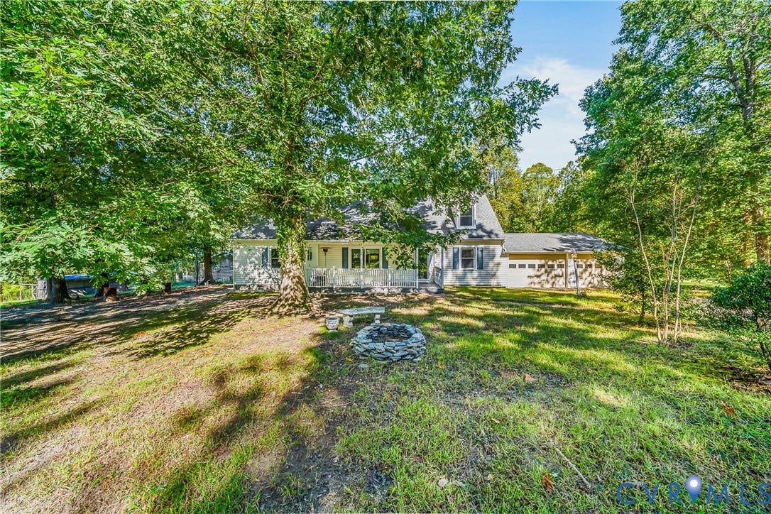 Exterior featuring a stone fire pit, mature shade trees, a covered front porch, and an attached two-car garage