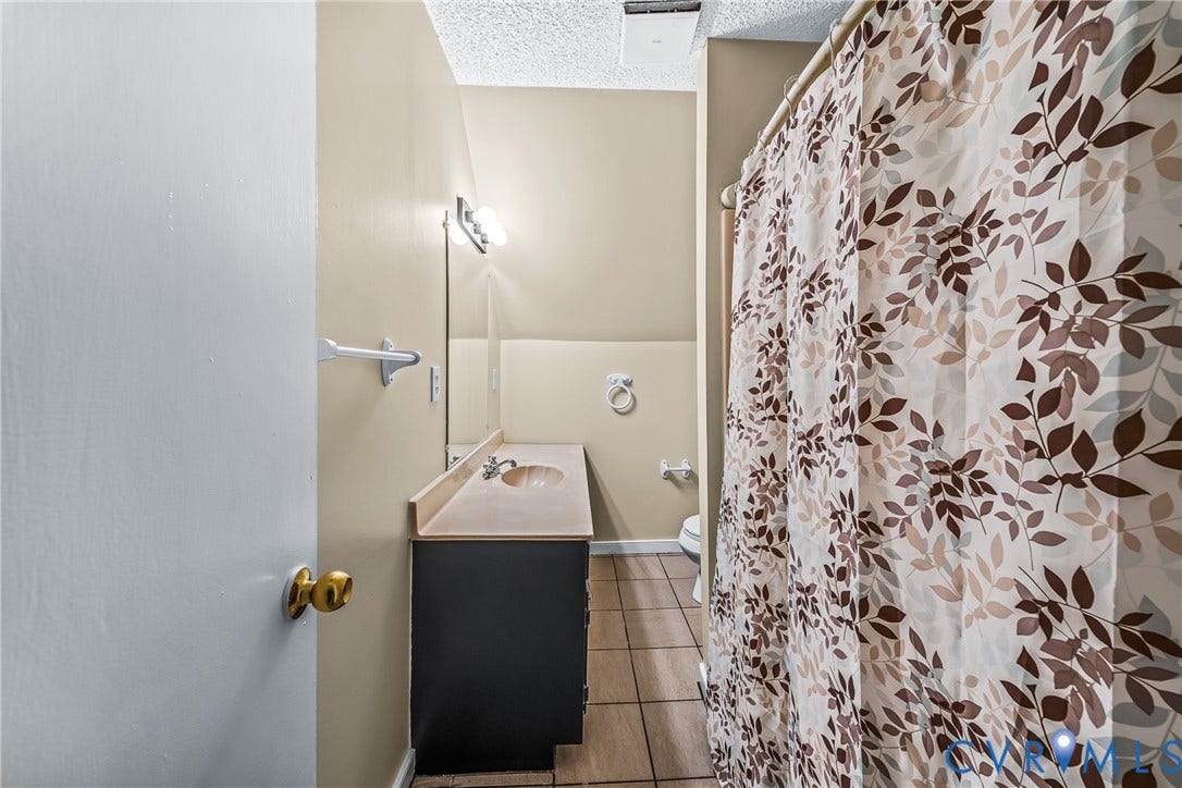 Bathroom featuring a single vanity with an integral sink, tile flooring, and a shower with a privacy curtain