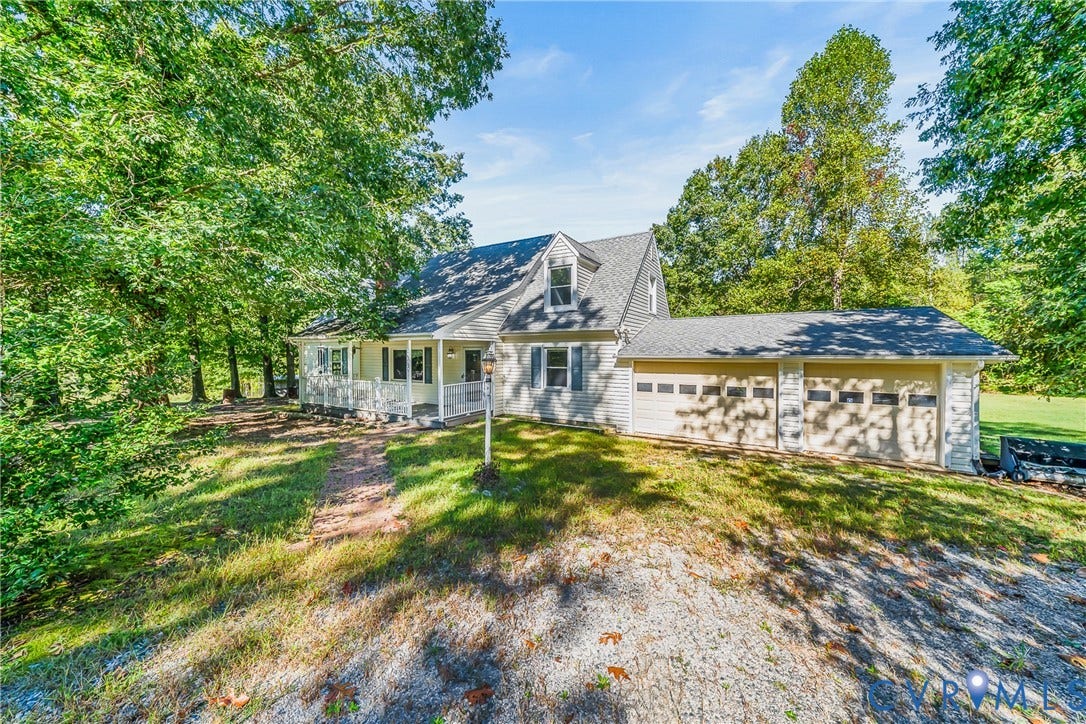 Expansive gravel driveway, attached two-car garage, dormer windows, covered front porch, and mature trees