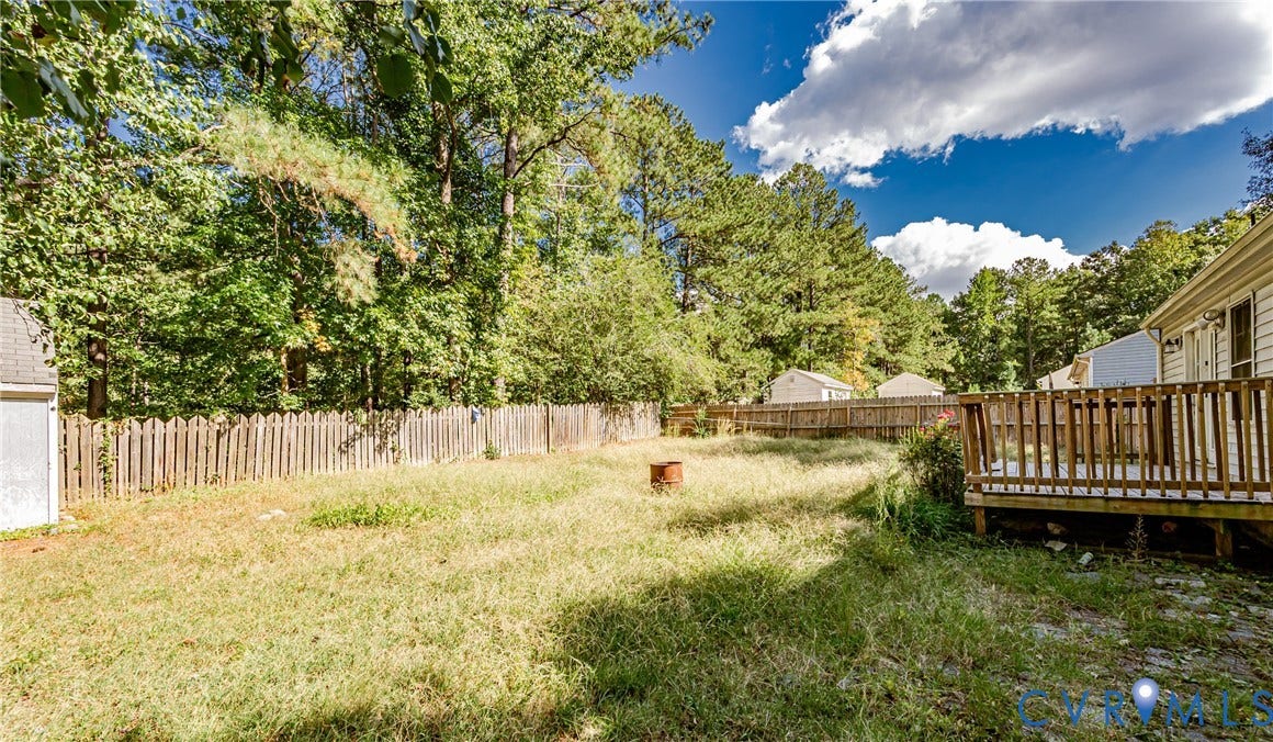 Expansive backyard featuring a wood deck, wood privacy fencing, mature trees, and a storage shed