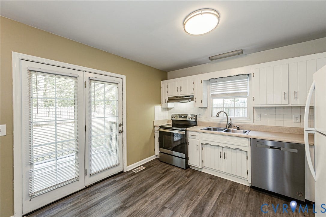 Kitchen featuring wood-finish flooring, white cabinetry, stainless steel appliances, and a double-basin sink