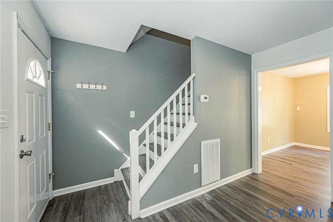 Entryway featuring wood-finish flooring, a paneled front door with decorative glass, and a white staircase with a contrasting gray runner