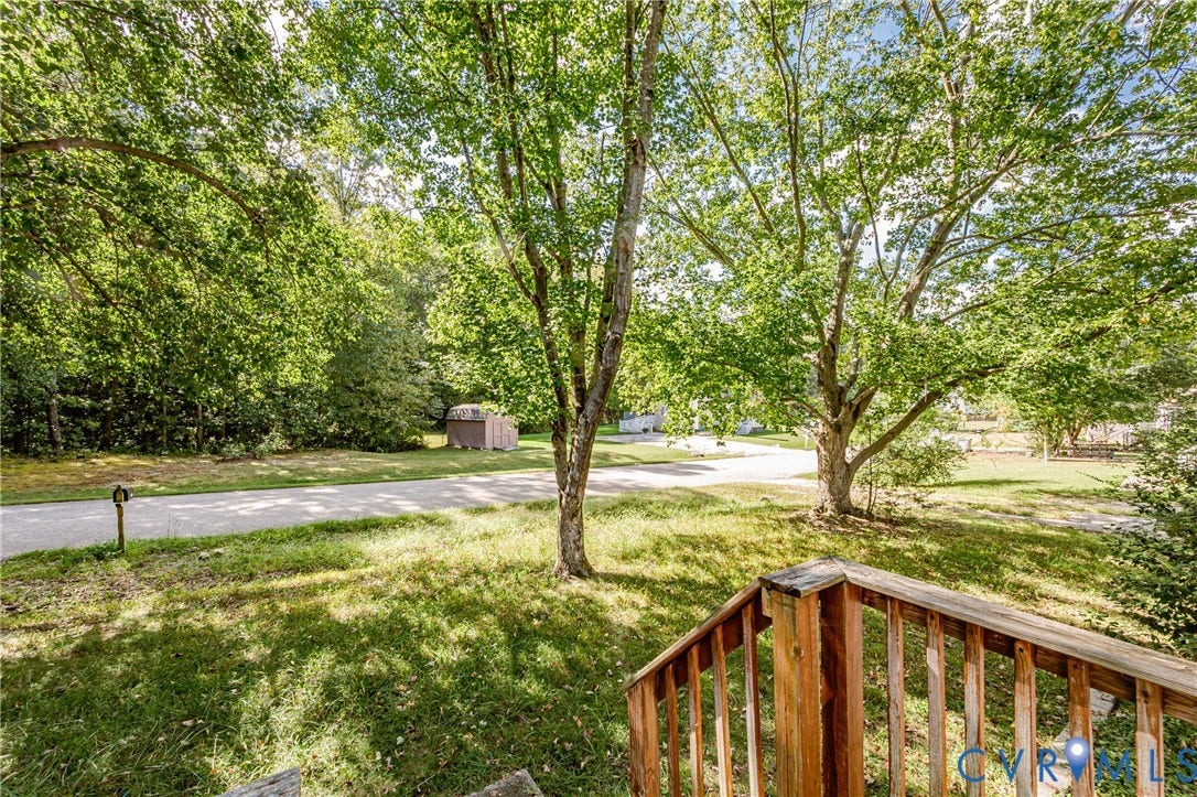 Expansive green space featuring a paved road, mature trees, and a wooden handrail