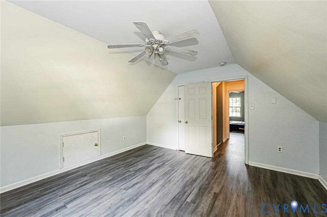 Sloped ceiling room featuring wood-finish flooring, a ceiling fan, and bi-fold closet doors