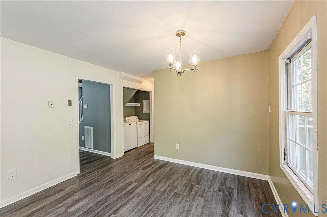 Wood-finish flooring, overhead chandelier, white trim, and a window with white casing