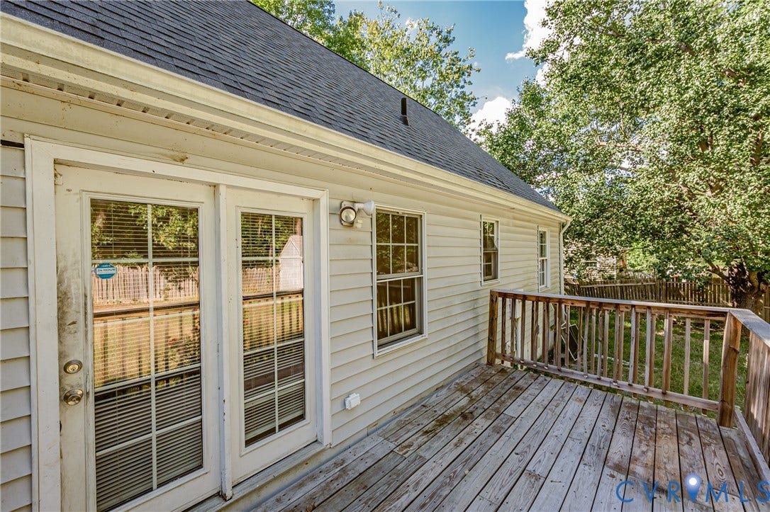 Exterior siding with multiple windows, leading to a wooden deck with railing