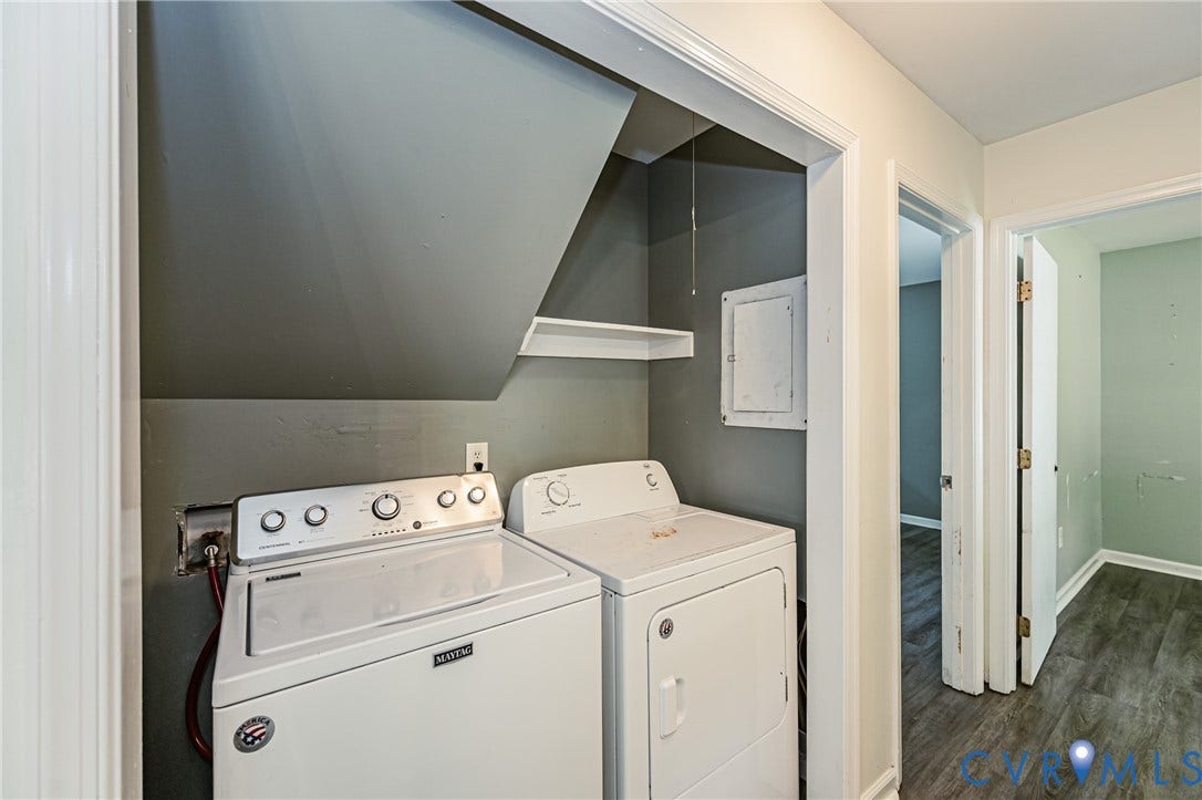 Dedicated laundry room featuring side-by-side washer and dryer with white enamel finish, overhead ventilation hood, enclosed storage shelving with dark accent wall, and direct access to adjacent spaces via multiple doorways