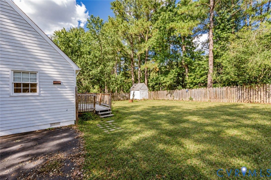 Expansive grassy lawn with a wooden privacy fence, mature trees, a detached storage shed, and a raised wood deck with steps