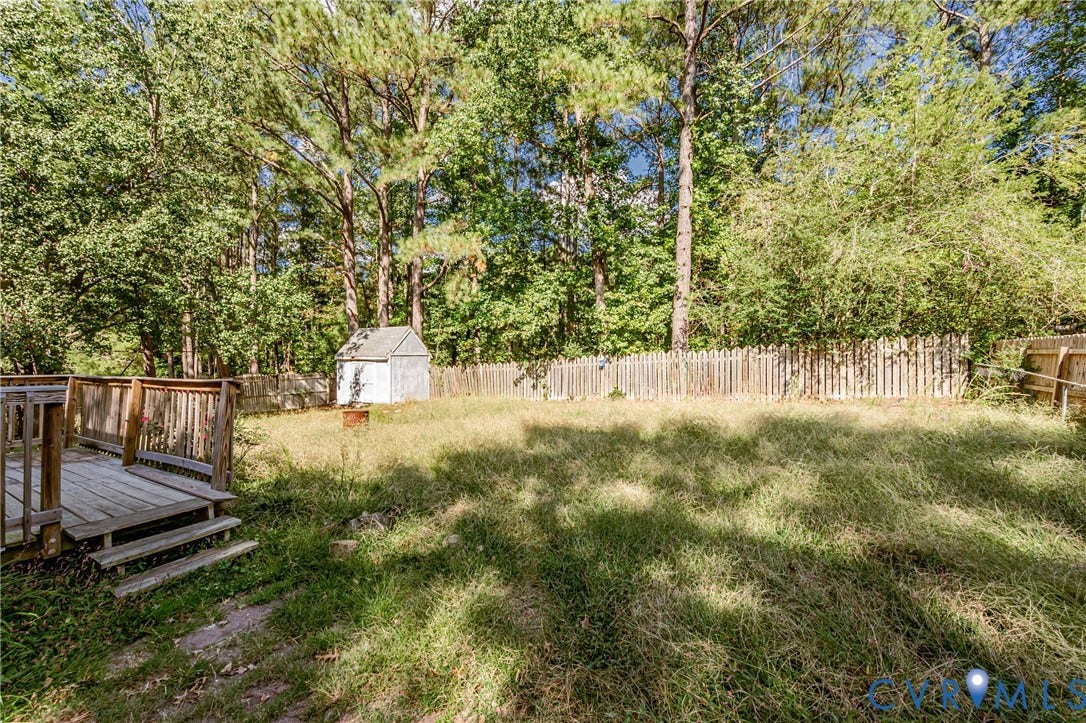 Expansive backyard featuring a wood deck with railings, a white storage shed, and a wooden picket fence