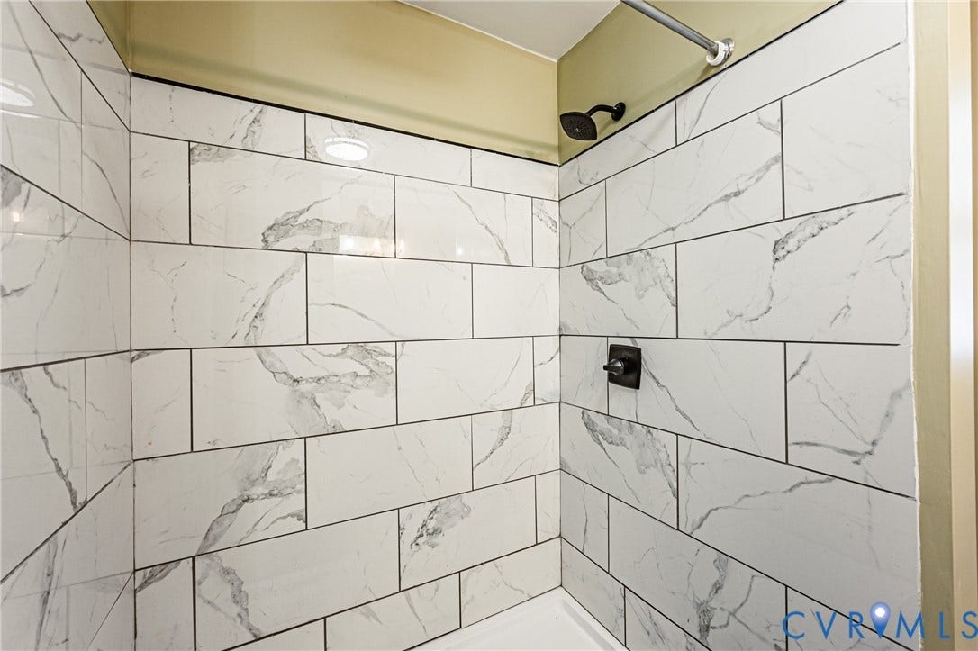 Shower enclosure with subway-style tile featuring a white and gray pattern, contrasting dark grout, and a matte black shower head and control
