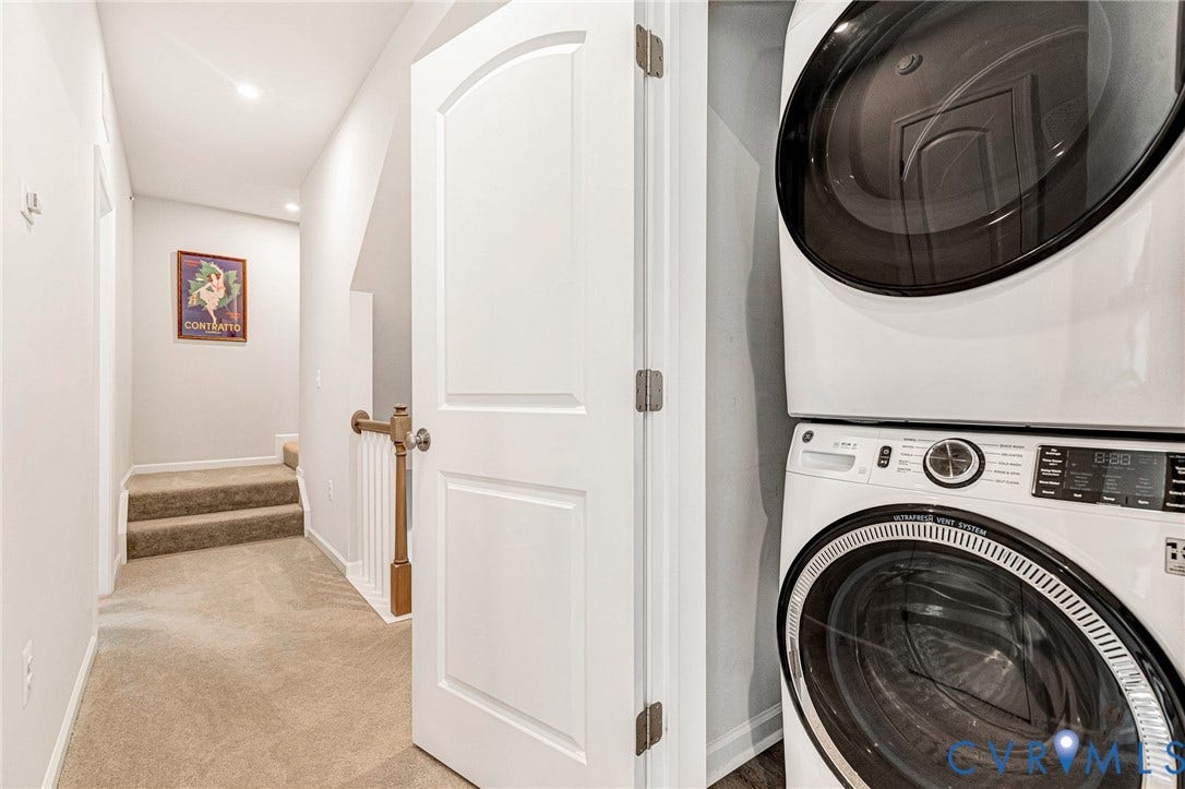 Stacked washer and dryer unit, arched interior door, carpeted flooring, recessed lighting, and wooden handrail