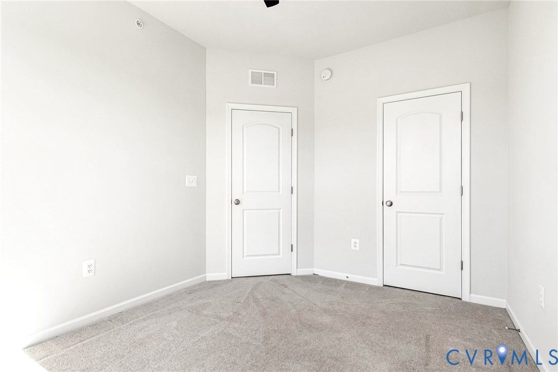 Carpeted room featuring light gray walls, white trim, and two paneled doors with arched top lites