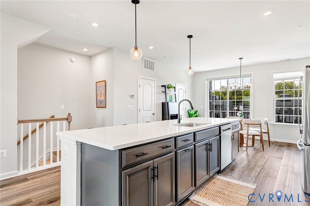 Kitchen island with a white countertop and dark gray cabinetry, wood-finish flooring, staircase with wood handrail, recessed lighting, and large windows